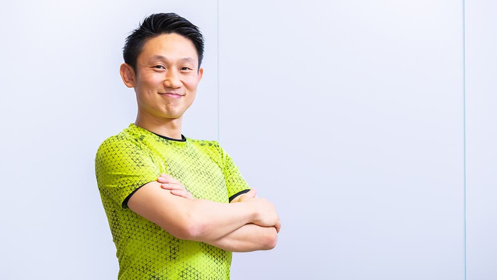 黄色の半袖シャツで姿勢よくこちらを向く佐々木泰士 アスリーダーズ株式会社代表取締役