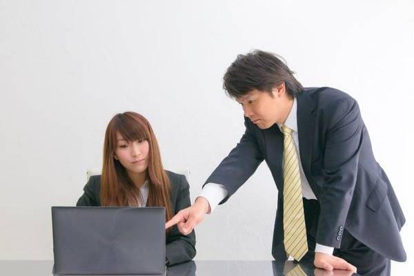 パソコンの前で説明をする男性社員とその話を聞く女性社員