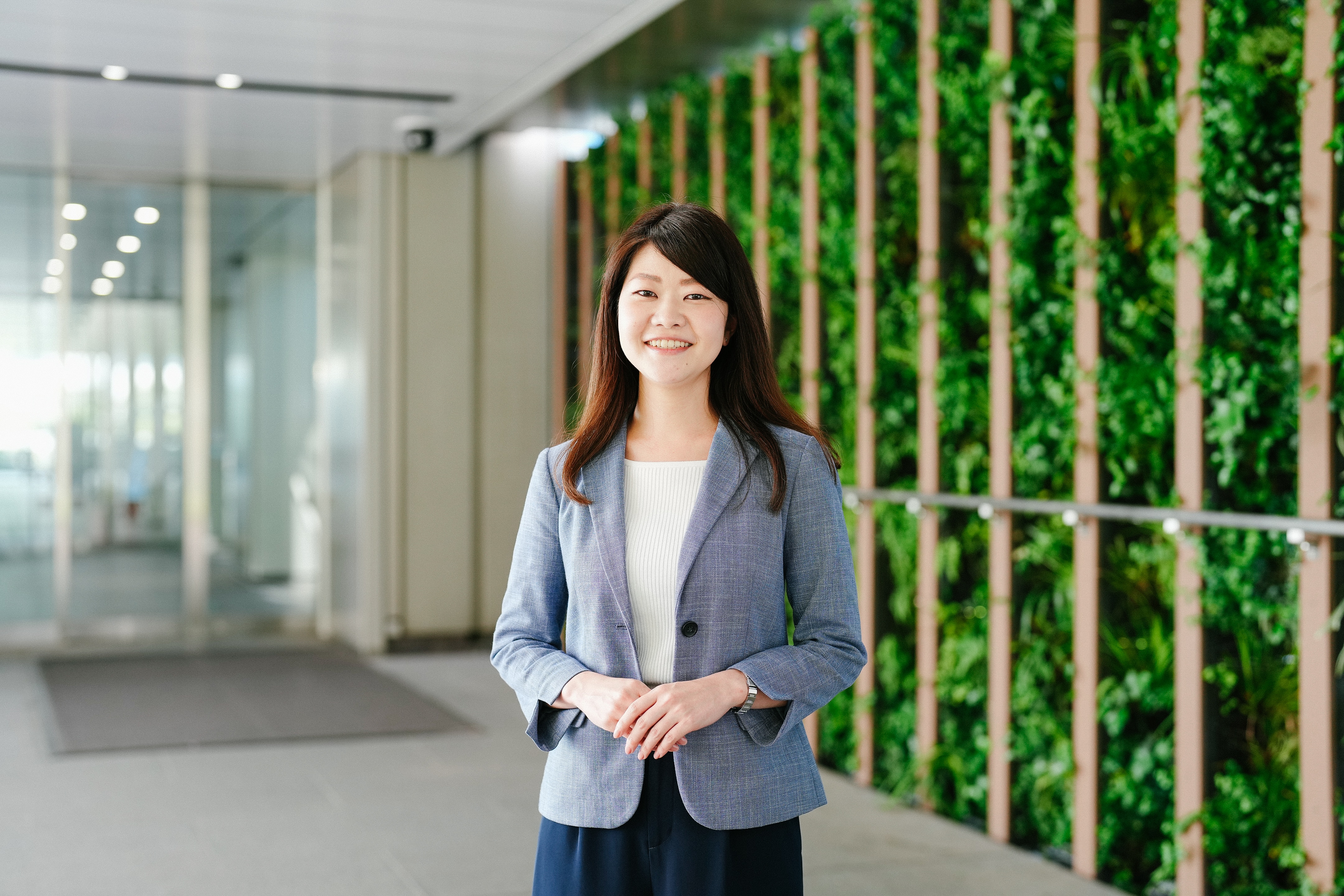 浜松町ビルの玄関に立っている、治験事務局担当者（SMA）のTさん