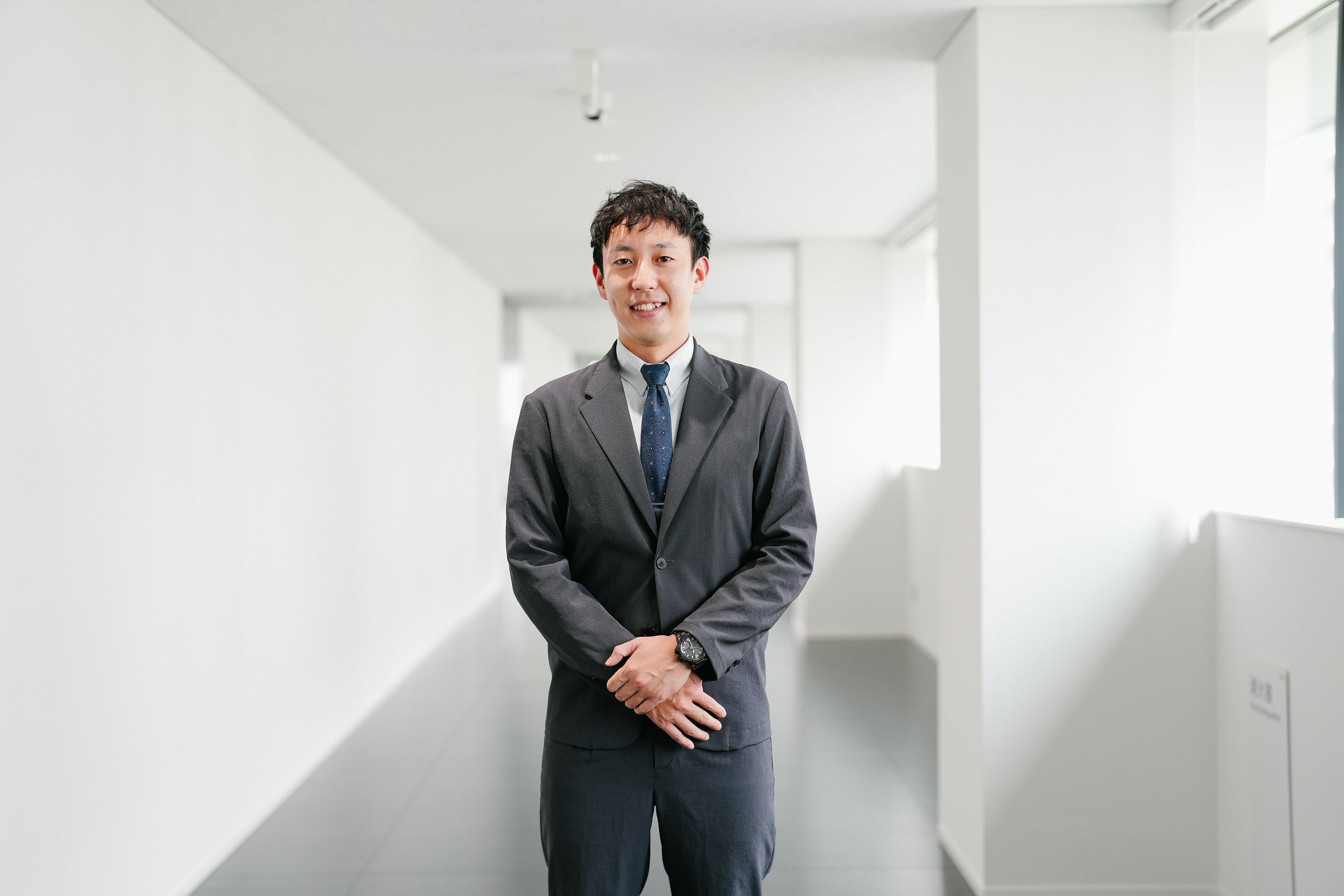 スーツを着て廊下に立っている、治験コーディネーター（CRC）の男性社員。