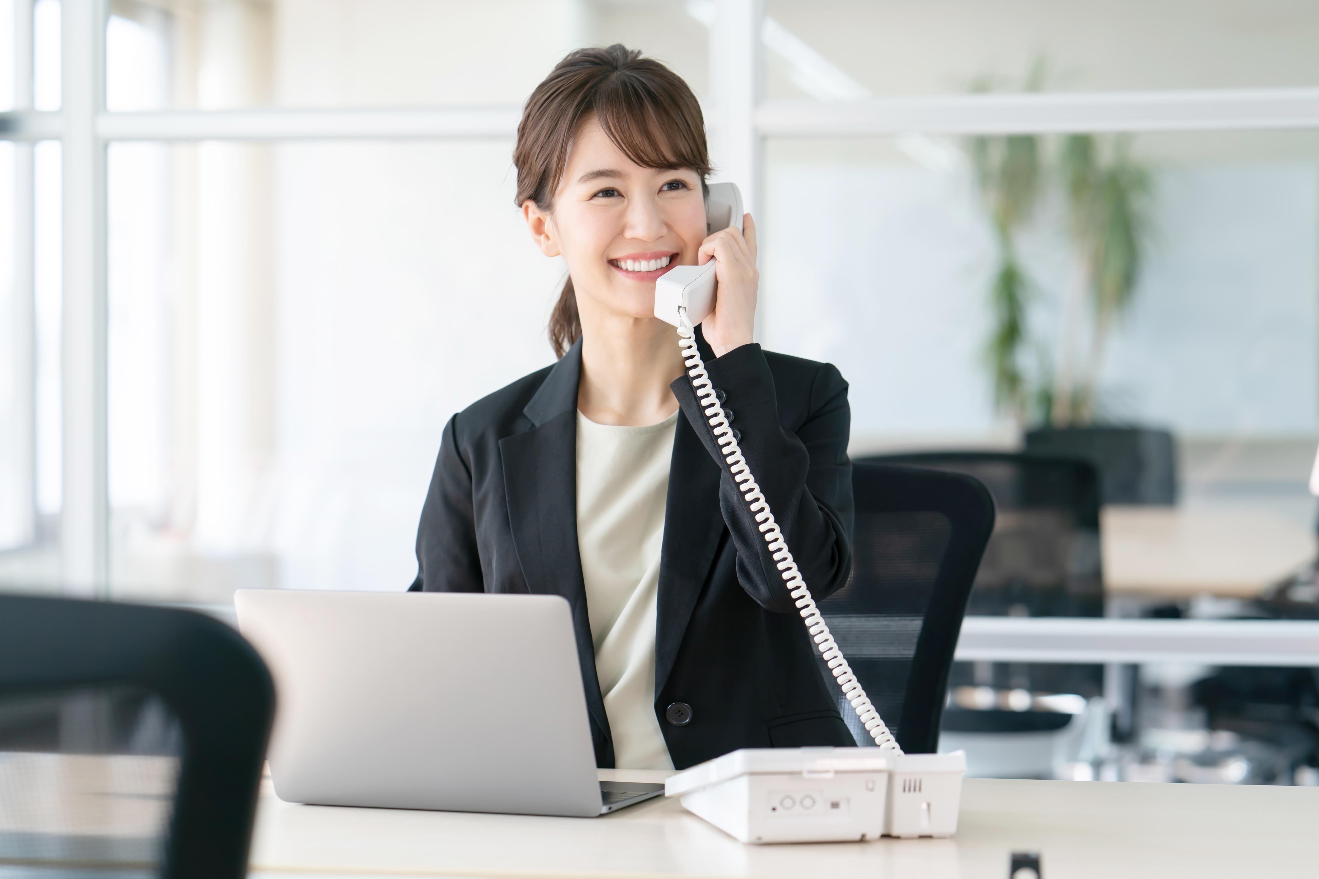 ノートパソコンを開いて固定電話で話しているビジネスパーソンの女性