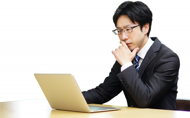PCの前で悩んでいる男性の写真