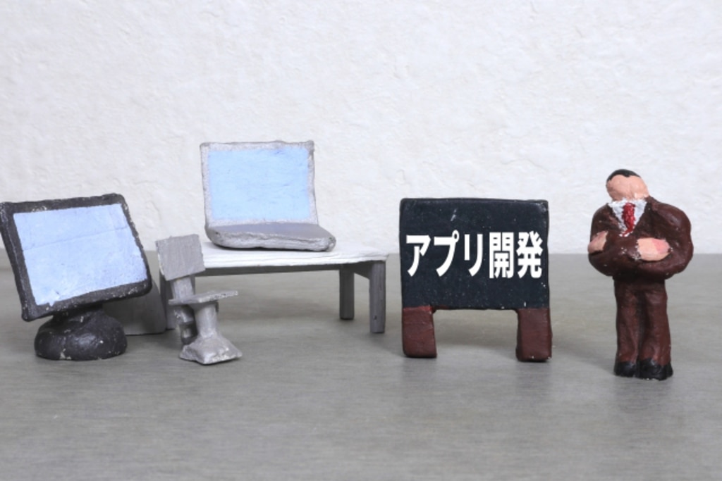 アプリ開発と書かれた黒板と首をかしげている男性の紙粘土