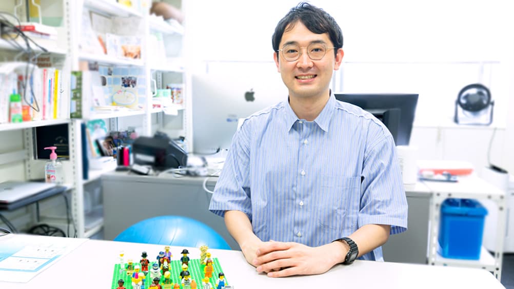 小型の人物モデルを机に並べた、舘野 泰一立教大学経営学部准教授(学際情報学博士)