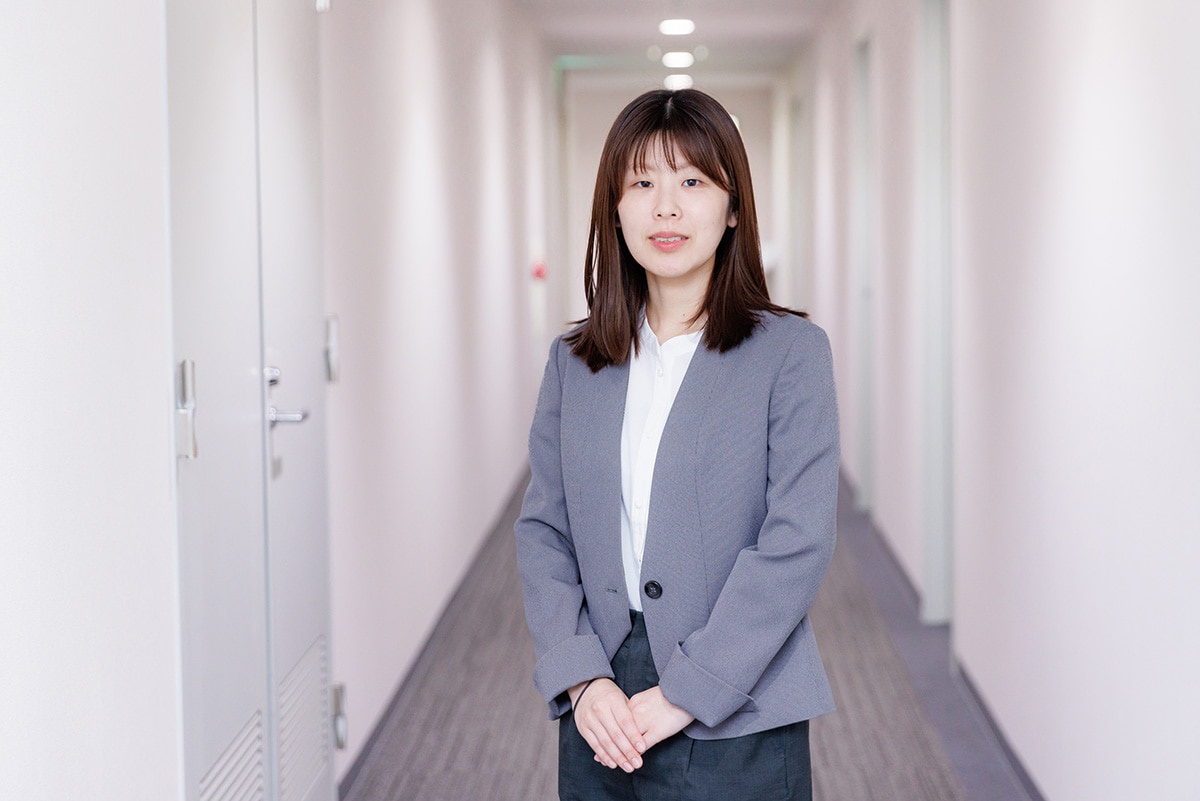 広島オフィスの廊下でスーツを着て立っている、治験コーディネーター（CRC）のOさん