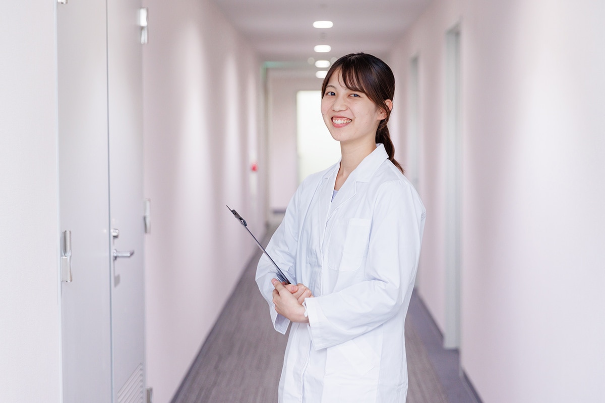 広島オフィスの廊下で白衣を着てバインダーを持っている、治験コーディネーター（CRC）のTさん