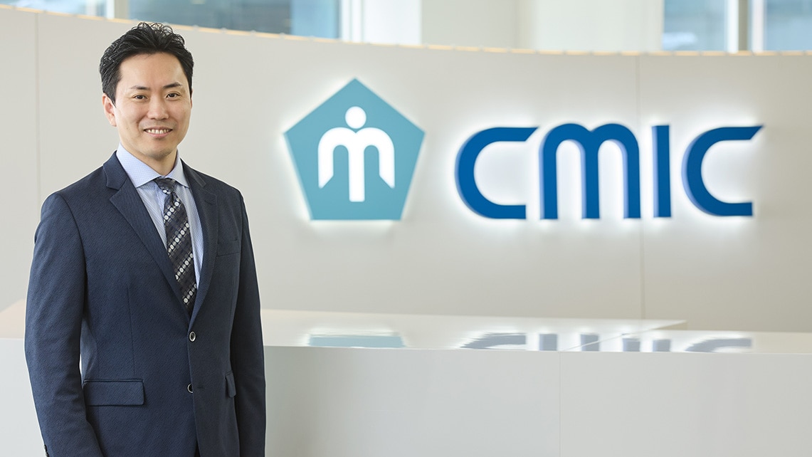 シミックグループの受付カウンター前に立っている、取締役副社長の坂﨑 孝平。事業企画本部 本部長、リソースマネジメント本部 本部長