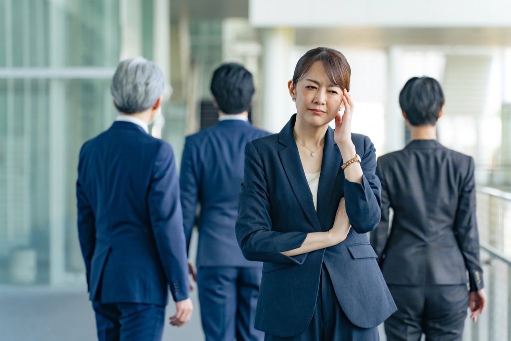 同僚に背を向けて悩むミドル女性ビジネスパーソン