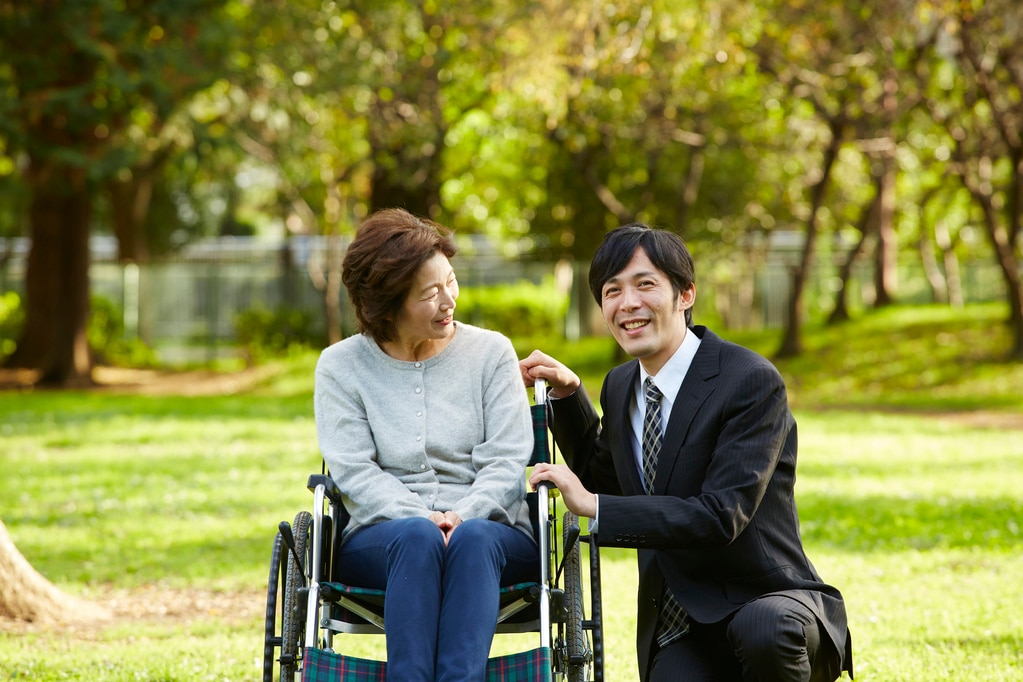 車いすに乗る母親に寄り添う会社員の息子