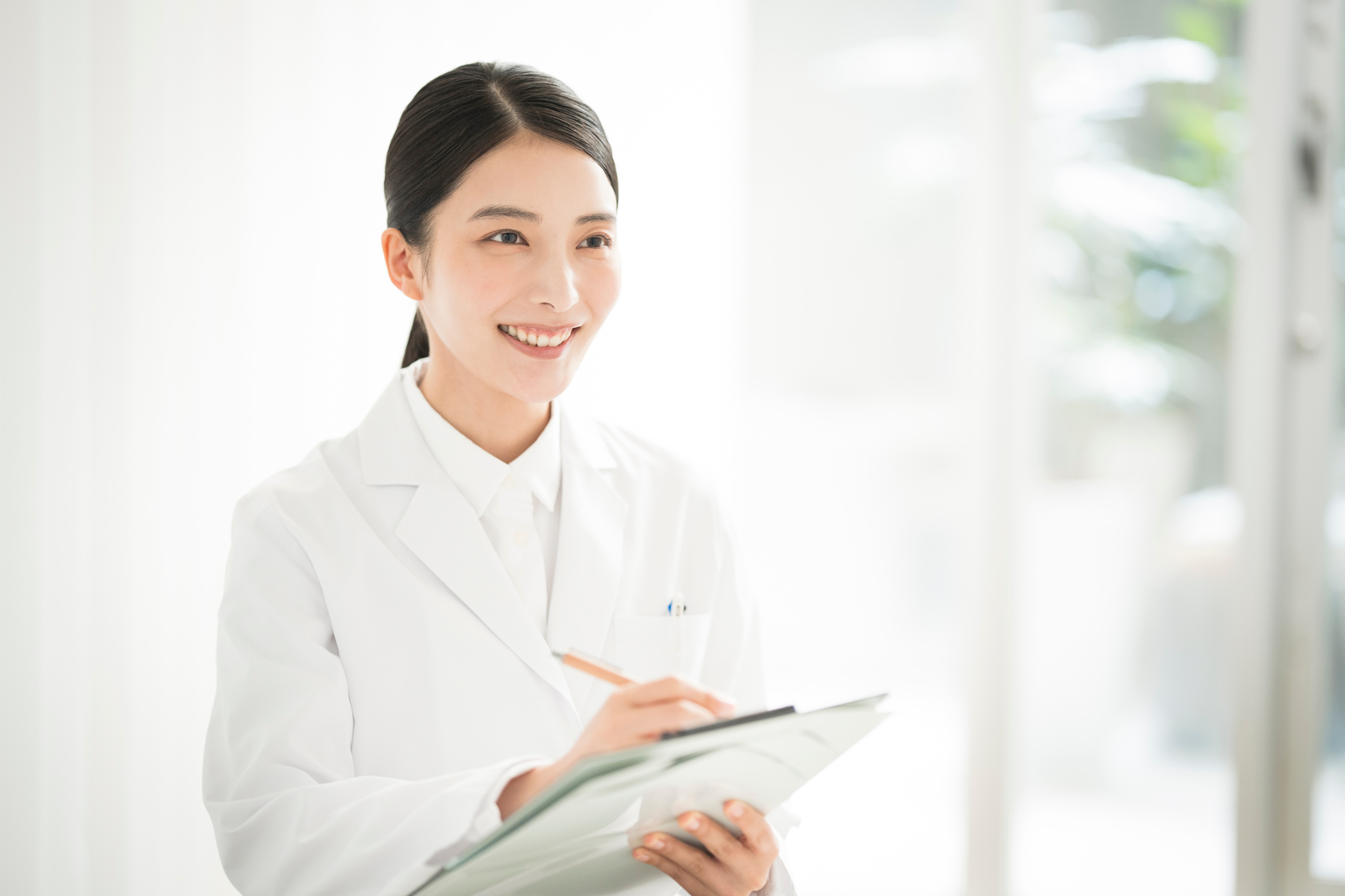 バインダーを持って相手の話を聞いている、白衣を着た治験コーディネーター（CRC）の女性