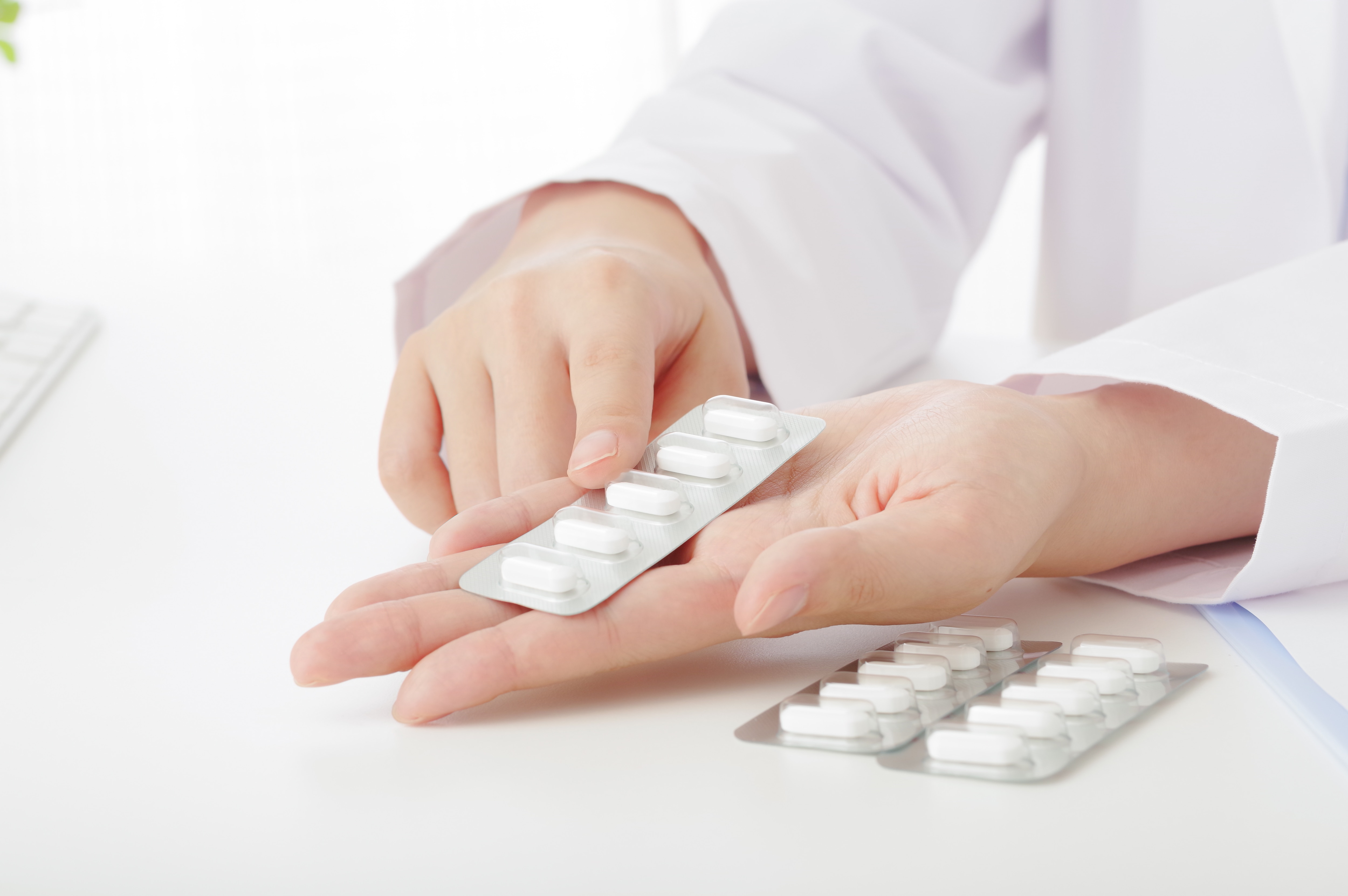 薬の錠剤のパッケージを手に取って説明する薬剤師の手元