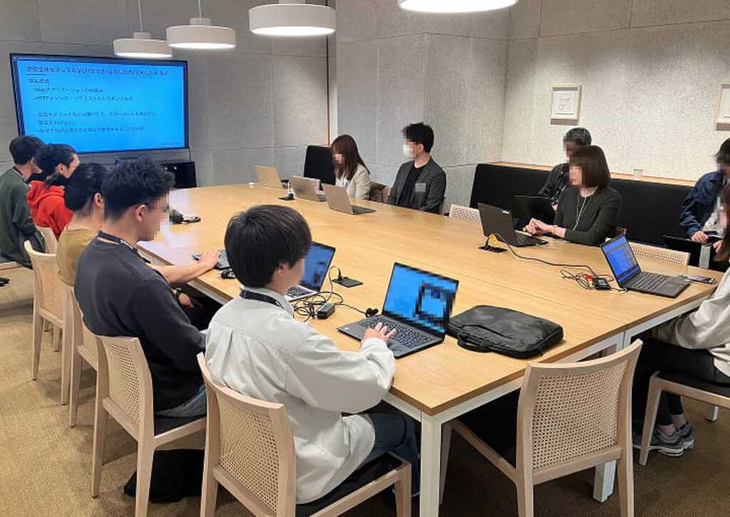 企業向け新入社員研修の様子。広々とした研修室で、受講生たちが各々ノートパソコンを使いながら真剣に講師の話に耳を傾けている場面。