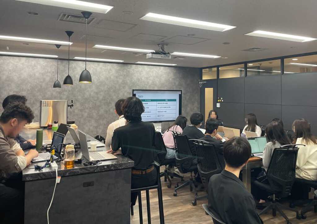 企業研修風景。集中力を高める環境で、新入社員が少人数グループでモニターを活用し、実践的な演習に取り組む様子。