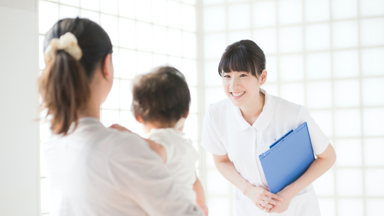 医療・福祉現場でのマナー研修イメージ。白衣姿のスタッフが青いバインダーを持ち、患者家族に礼儀正しく応対する様子。