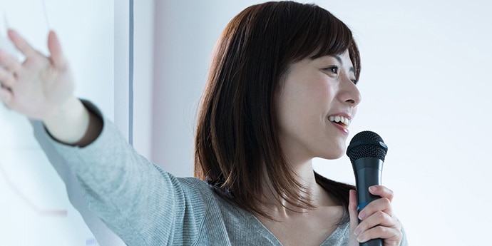 女性活躍推進研修 女性リーダー育成イメージ。マイクを持ち、前方に向かって説明する人物を通じて、リーダーシップや指導力を表現した写真。