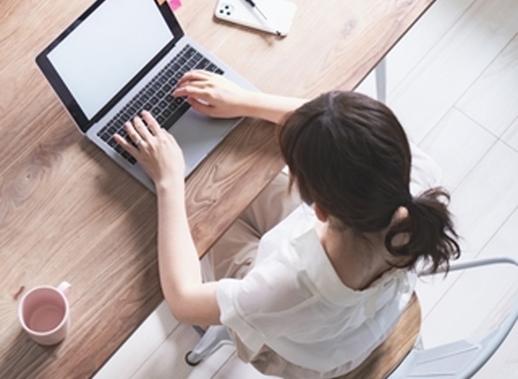 テレワーク対応の新入社員ビジネスマナー研修イメージ。自宅でノートPCを使いオンライン業務を行うデスクとスマートフォン、ノート、カップ。