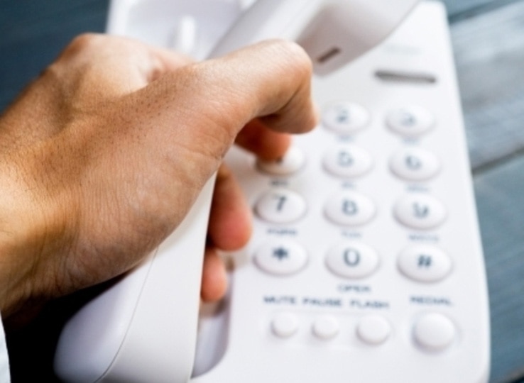 電話応対研修イメージ。ビジネスシーンで白い固定電話の受話器を取る手元、信頼感を伝える応対スキル習得を表現。