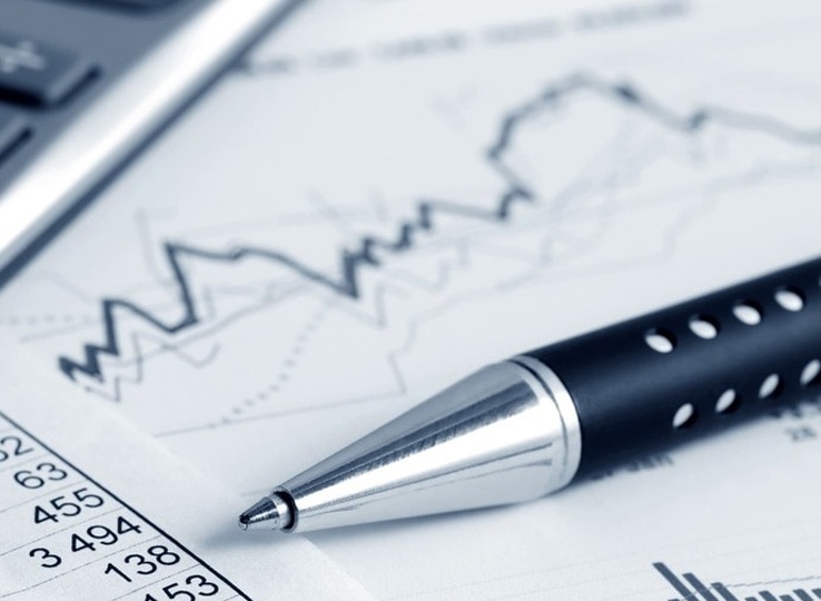 ビジネス文書研修のイメージ。財務資料やグラフを確認しながら報告書やメールを作成するためのデスクに置かれた電卓とペン。