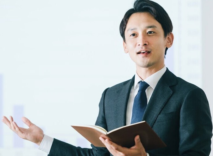 第一印象を高める自己演出研修イメージ。スーツ姿でノートを持ち、棒グラフを背景に信頼感を演出するプレゼンテーションの様子。