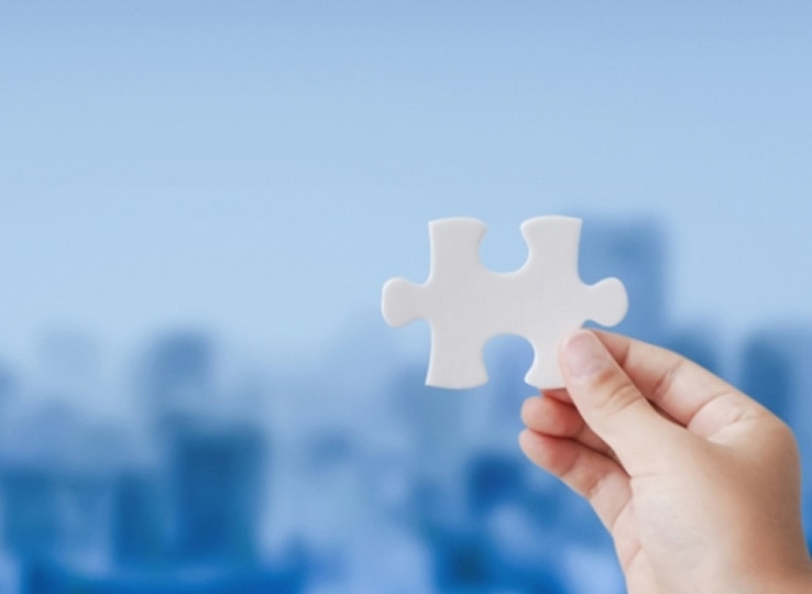 青い背景を背に、手に持った白いジグソーパズルのピースが映っている。