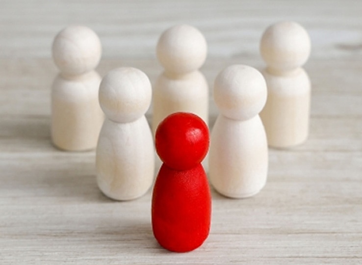 木製の駒が並ぶ中、中央に赤い駒が立っている様子。白い駒が周囲に配置され、リーダーシップ研修を象徴する、チームを率いる存在を示すイメージ。