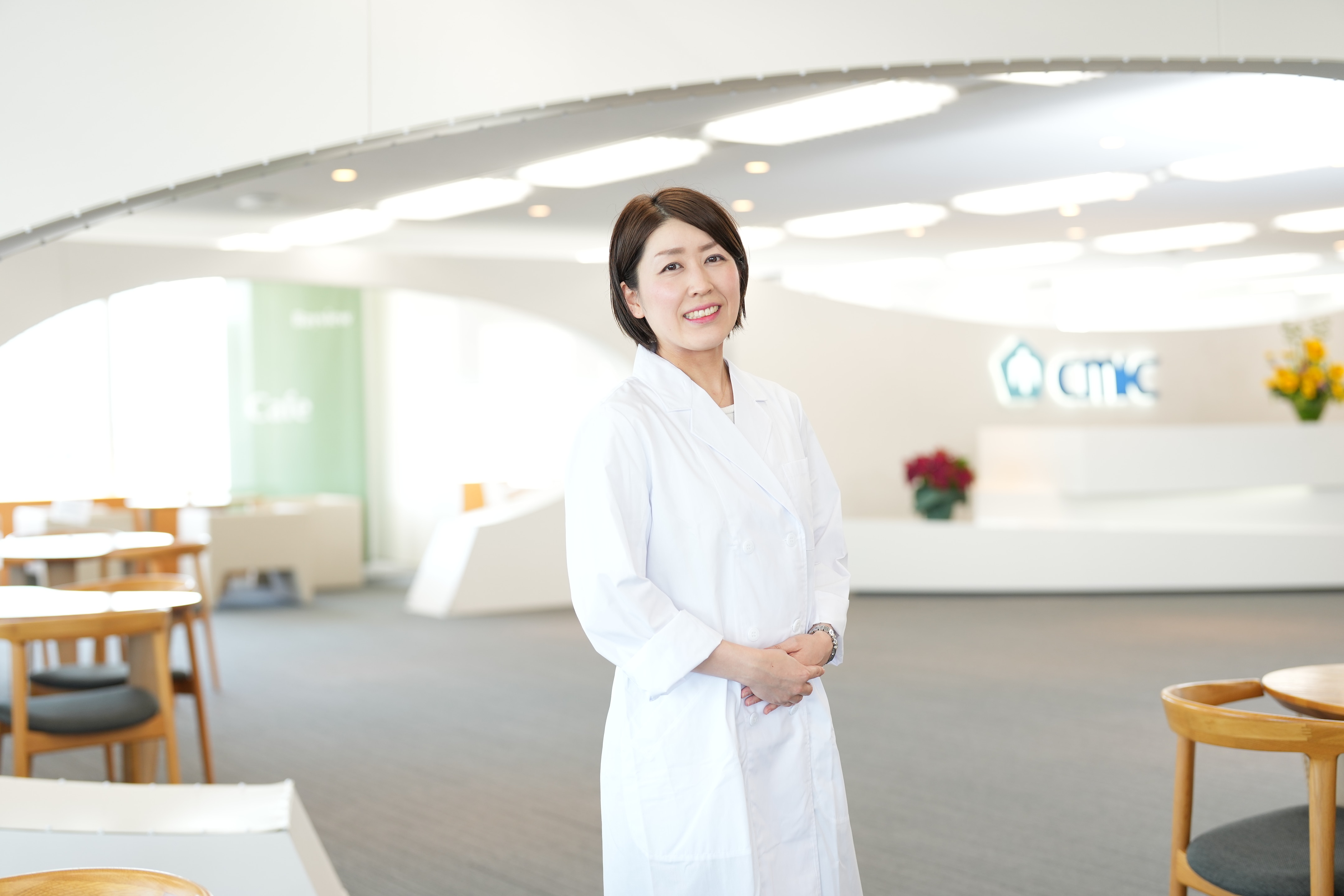 白衣を着て、シミックグループの受付前に立つ、治験コーディネーター（CRC）のM.Sさん