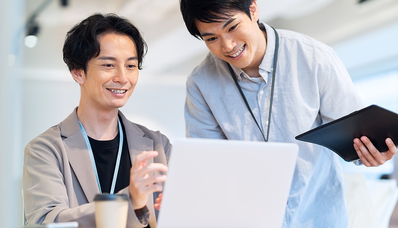 話している人物と、机上のノートPCに向かう複数の社員の写真。