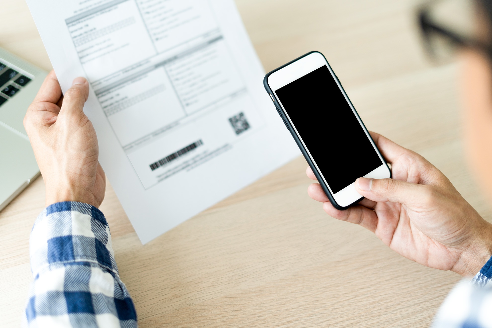 紙に印字された二次元コードをスマートフォンで読み取る手元