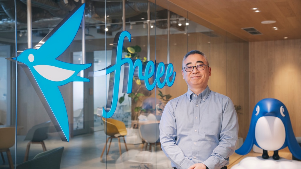 freeeのロゴやキャラクターと並んで立ち、今後の展望について笑顔を見せる米世毅氏