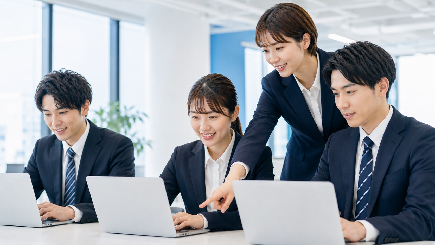 明るくモダンなオフィスで、3人の若い日本人新入社員がノートパソコンを使って学んでいる写真