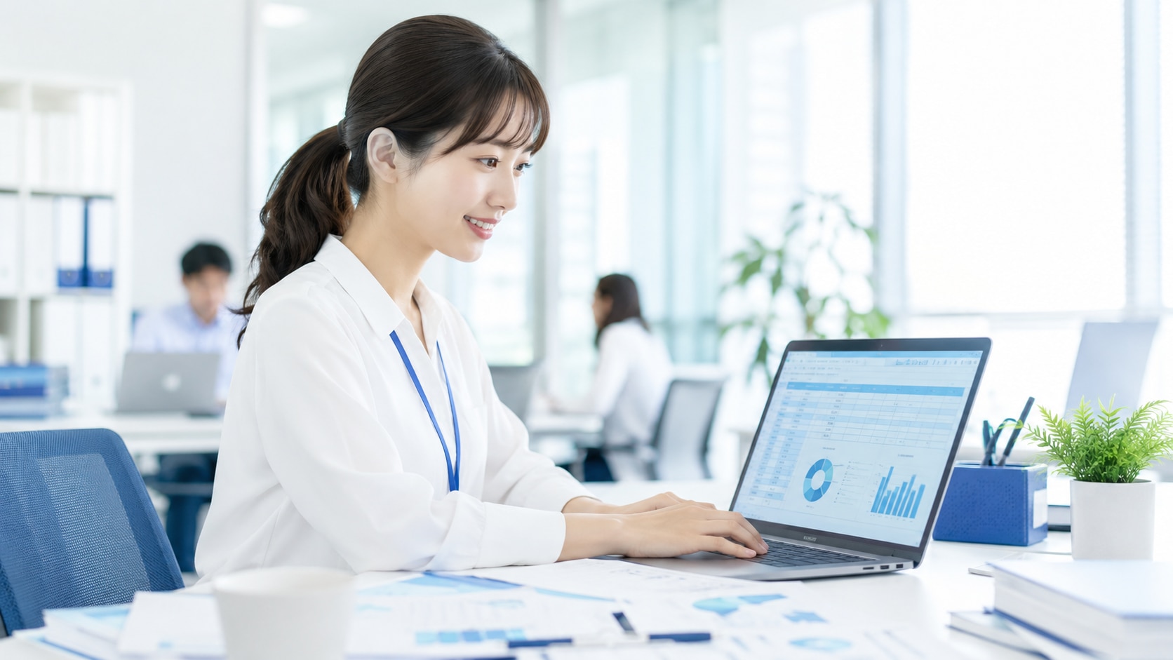 明るいオフィスで、新入社員が研修で学んだExcelスキルを使い、実際の業務書類(日報や帳票)を作成している様子