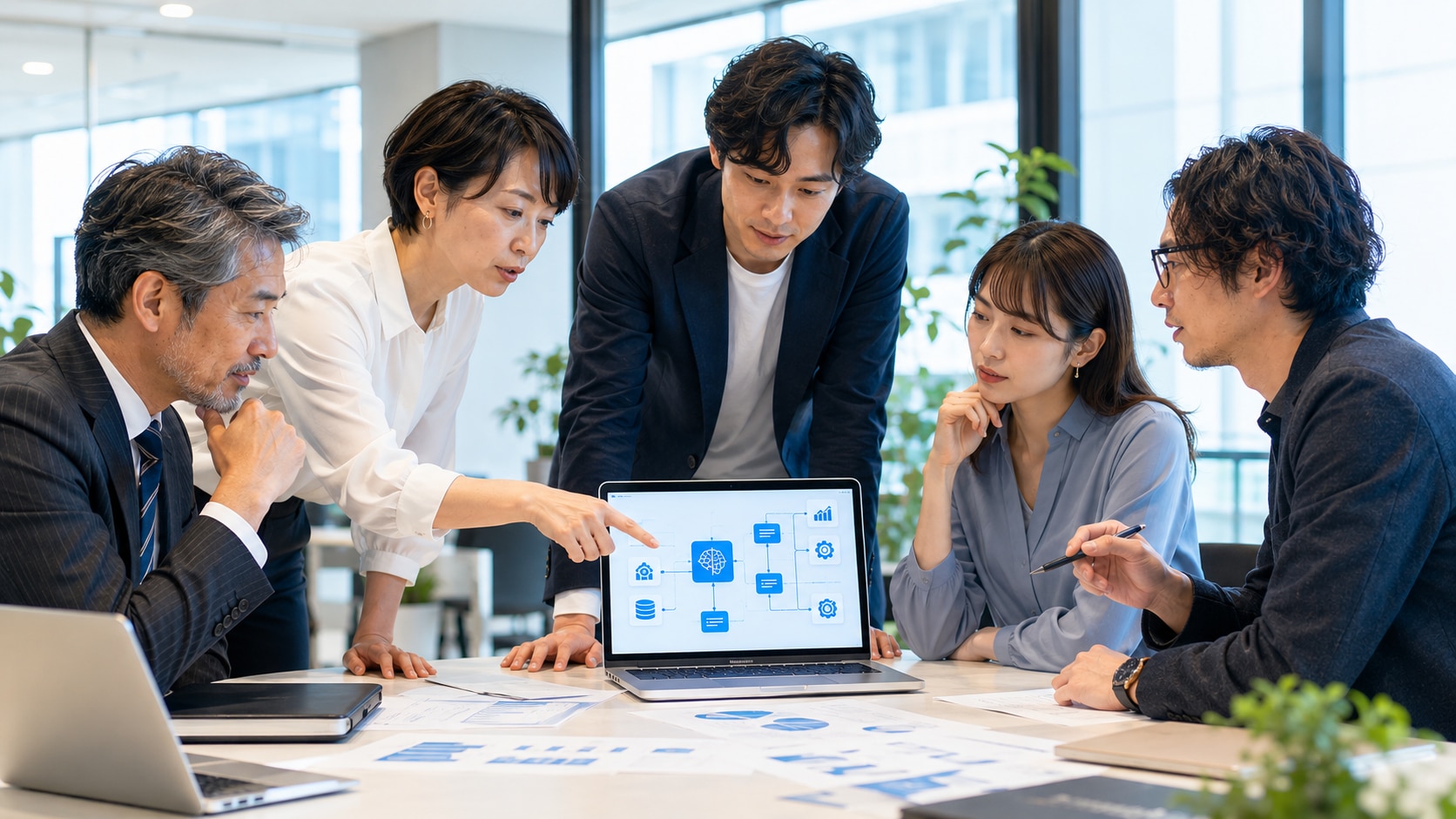 多様な日本人のビジネスチームが、AIのワークフロー図が表示されたノートパソコンを囲んで議論している