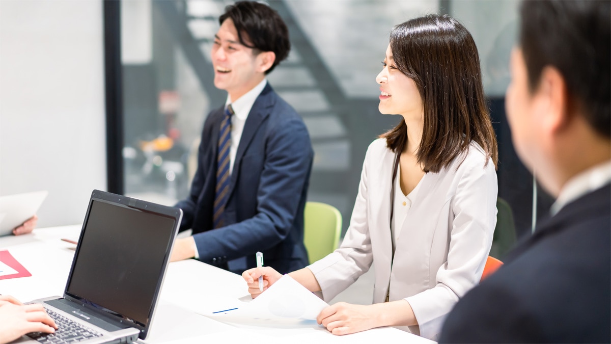職場の会議で複数の社員が資料をもとに話し合う様子。ハラスメント研修、パワハラ防止、職場コミュニケーション改善、心理的安全性の向上をテーマとしたビジネスシーン