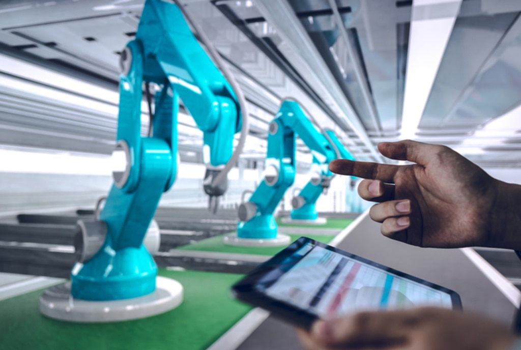 ロボットアームが並ぶ生産ラインをタブレットで操作する様子