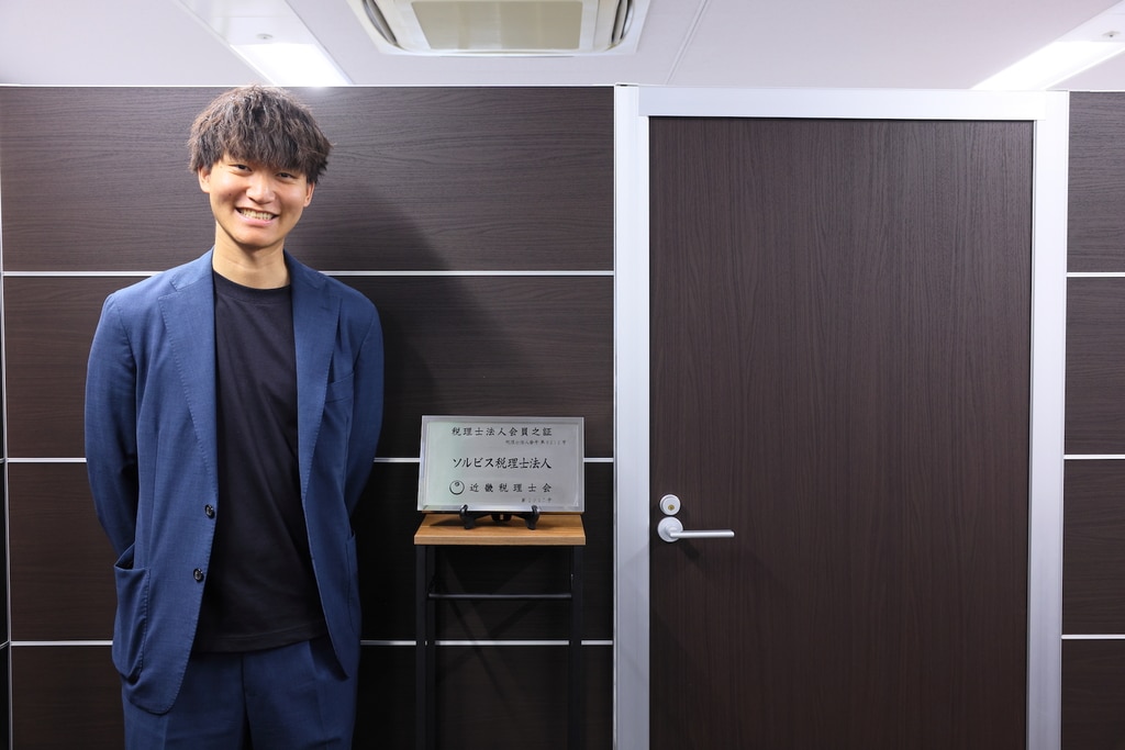 ソルビス税理士法人オフィスの看板の横に立つ代表の境裕介氏