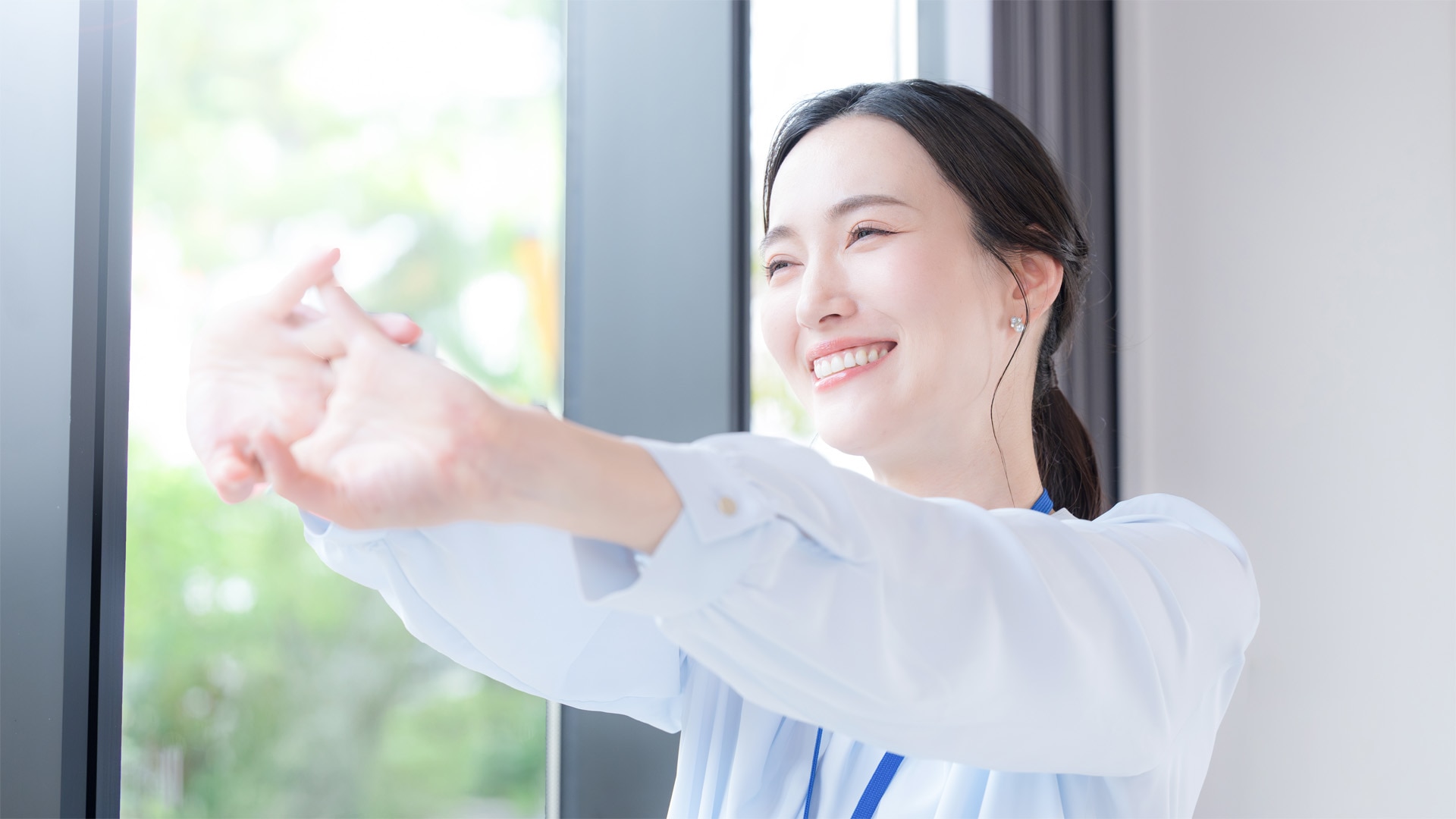女性活躍推進・健康経営支援サービス「生理痛体験ワークショップ」&「フェムテック」|健康的な女性がオフィスの窓辺でストレッチをしている風景